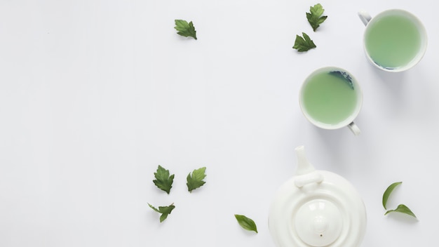 Tè verde fresco con le foglie di tè e la teiera su fondo bianco