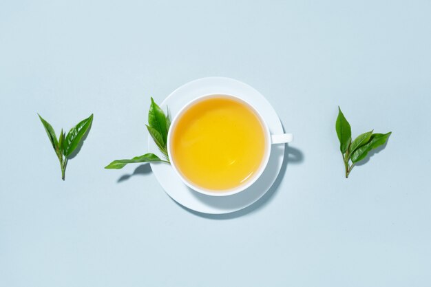 Tè verde preparato in tazza con foglie di tè su sfondo blu pastello. Vista dall'alto.