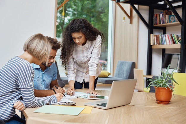 Team di giovani imprenditori creativi che lavorano al progetto di gruppo, guardando attraverso informazioni sui profitti sul computer portatile, scrivendo idee su carta. Concetto di brainstorming.