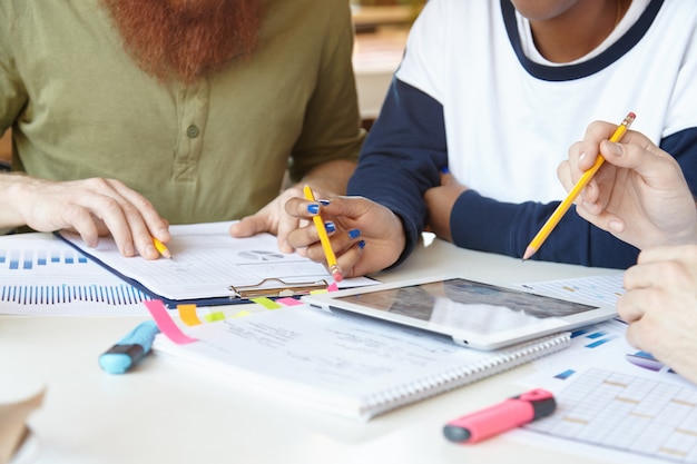 Team multietnico di giovani partner che si incontrano alla caffetteria, discutono di piani, condividono idee, analizzano i dati finanziari del progetto utilizzando il laptop.