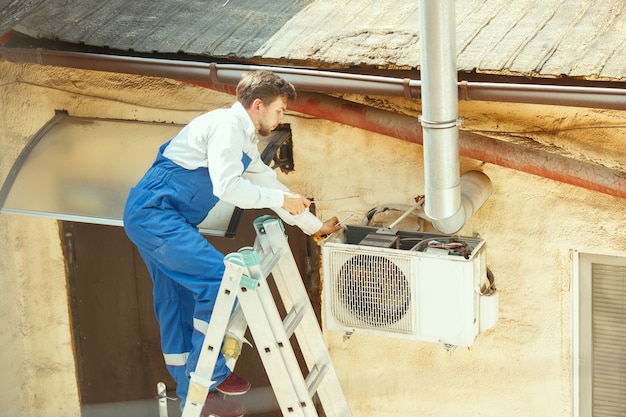 Tecnico HVAC che lavora su una parte del condensatore per l'unità motocondensante. Operaio o riparatore di sesso maschile in uniforme che ripara e regola il sistema di condizionamento, diagnostica e cerca problemi tecnici.