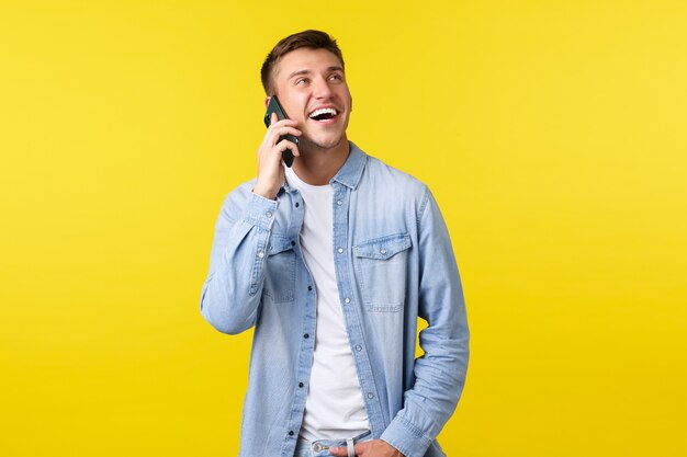 Tecnologia, concetto di stile di vita. Gioioso bell'uomo sorridente che ha una conversazione felice al telefono, chiama un amico, sembra entusiasta e tiene lo smartphone vicino all'orecchio, sfondo giallo.