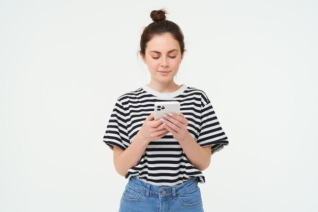 Tecnologia e stile di vita giovane donna in piedi su sfondo bianco con lo smartphone