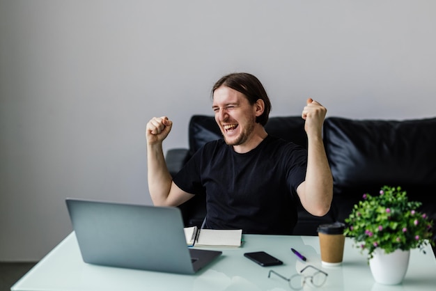 Tecnologia lavoro remoto e concetto di stile di vita uomo felice con computer portatile che celebra il successo in ufficio a casa