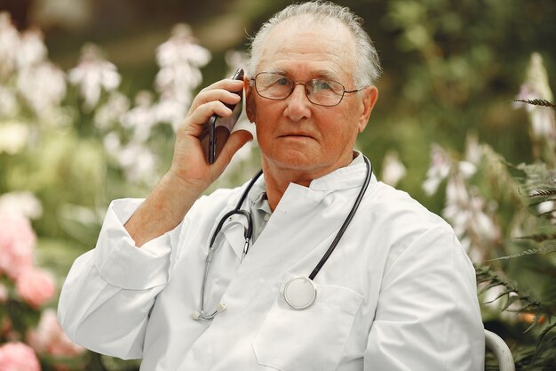 Tecnologia, persone e concetto di comunicazione. Uomo maggiore al parco estivo. Medico che utilizza un telefono.