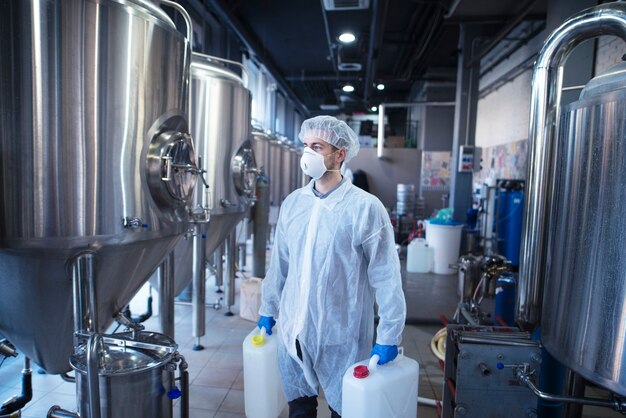 Tecnologo lavoratore industriale in possesso di contenitori di plastica in procinto di cambiare i prodotti chimici nella macchina per la lavorazione degli alimenti