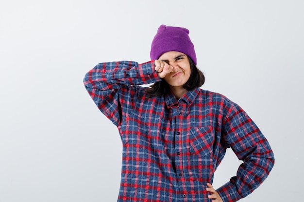 Teen donna strofinando gli occhi con il pugno e tenendo la mano sull'anca in camicia a quadri