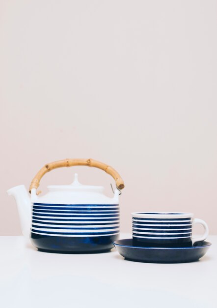 Teiera e tazza delle bande blu sullo scrittorio bianco contro fondo