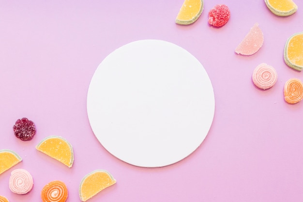 Telaio bianco circolare bianco con caramelle di zucchero di gelatina su sfondo rosa