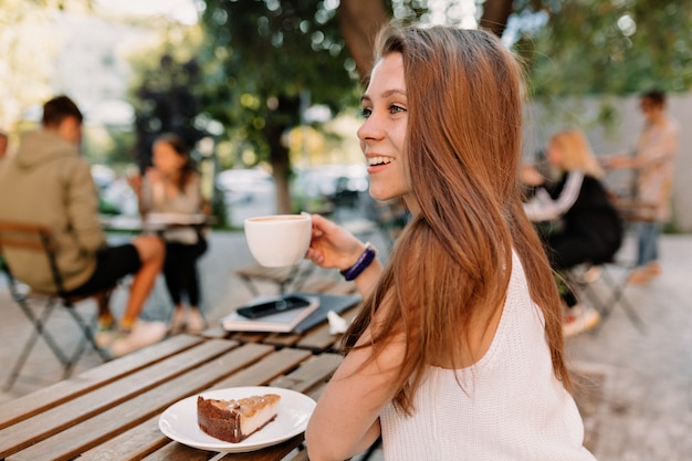 Telaio dal retro della giovane donna attraente con i capelli lunghi che beve caffè sulla terrazza estiva in una buona giornata di sole