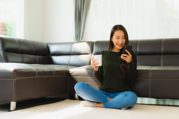 Telefono cellulare astuto di bello giovane uso asiatico asiatico della donna del ritratto con la tazza di caffè