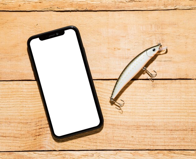 Telefono cellulare con display bianco e richiamo di pesca sulla scrivania in legno