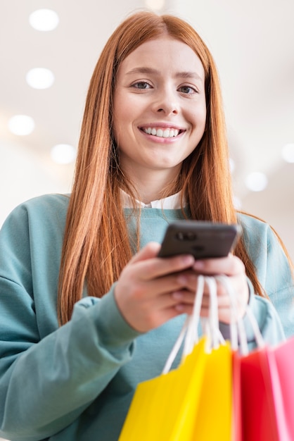 Telefono della tenuta della donna e sacchi di carta sorridenti