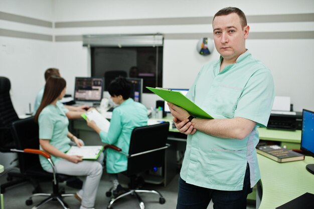 Tema medico Ritratto di medico di sesso maschile con appunti contro un gruppo di medici riuniti nell'ufficio di risonanza magnetica presso il centro diagnostico in ospedale