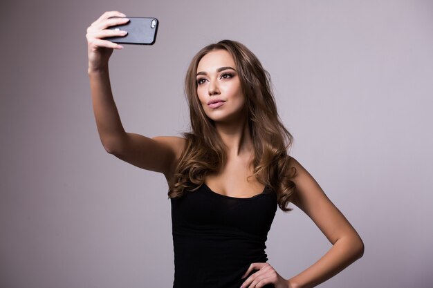 Tempo di selfie. Giovani donne allegre che fanno selfie dal suo telefono intelligente sul muro grigio