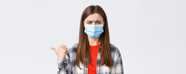 Tempo libero dell'epidemia di coronavirus sul concetto di distanza sociale ed emozioni in quarantena Giovane donna sconvolta e delusa in maschera medica accigliata condanna smth che punta il dito a sinistra scontenta