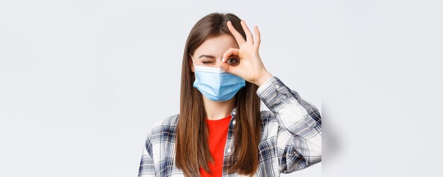 Tempo libero per l'epidemia di coronavirus in quarantena concetto di distanza sociale ed emozioni Il primo piano di una donna ottimista di bell'aspetto in maschera medica mostra segno e strizzatina d'occhio ok