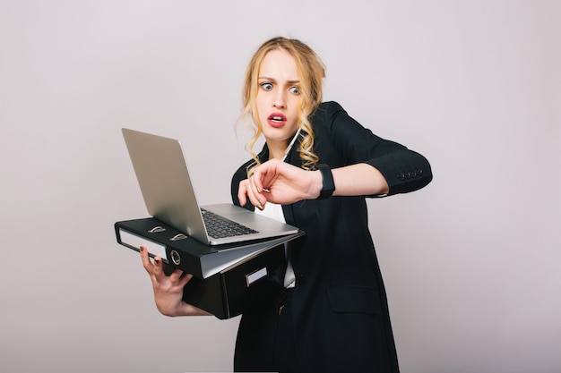 Tempo occupato ufficio di lavoro di giovane donna bionda in abiti formali con laptop, cartella parlando al telefono. Stupito, lavoro, professione, segretario, impiegato, manager