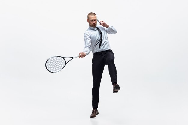 Tempo per il movimento. L'uomo in vestiti dell'ufficio gioca a tennis isolato su bianco. Addestramento dell'uomo d'affari in movimento, azione. Look insolito per sportivi, nuova attività. Sport, stile di vita sano.