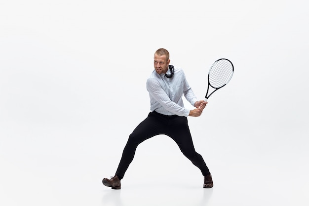 Tempo per il movimento. L'uomo in vestiti dell'ufficio gioca a tennis isolato su bianco. Addestramento dell'uomo d'affari in movimento, azione. Look insolito per sportivi, nuova attività. Sport, stile di vita sano.