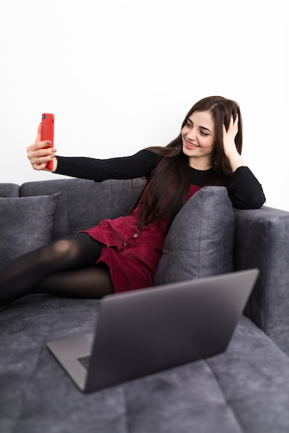 Tempo per selfie. Bella giovane donna che fa selfie con il sorriso mentre sedendosi sul sofà con il computer portatile sulle sue ginocchia nell'interno domestico