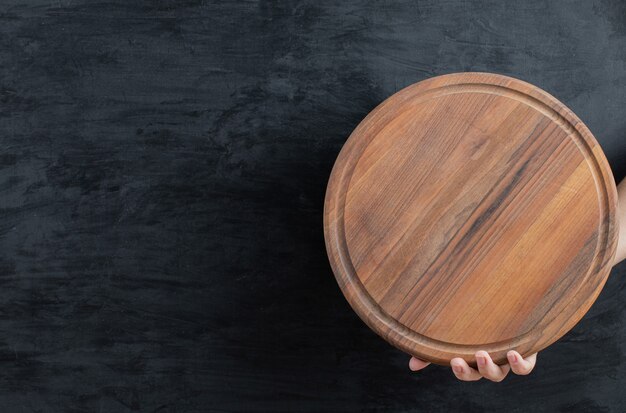 Tenendo in mano un piatto di legno su sfondo nero