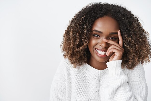 Tenerezza bellezza e puro concetto di emozioni Ritratto di sensuale tenera e carina ragazza afroamericana in maglione ridendo e ridacchiando carina come guardando la fotocamera tenendo le dita sulla guancia