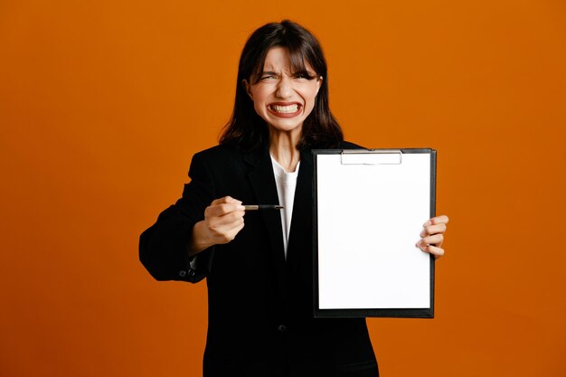 Tenuta tesa e punti con la penna negli appunti giovane bella donna che indossa una giacca nera isolata su sfondo arancione