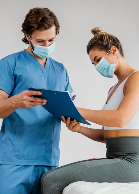 Terapista osteopatico maschio con maschera medica e paziente femminile negli appunti di firma dell'ufficio
