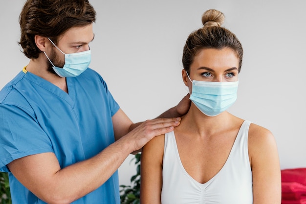 Terapista osteopatico maschio con mascherina medica che controlla il collo del paziente femminile