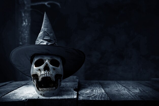 Teschio umano sul tavolo di legno con un cappello sullo sfondo scuro