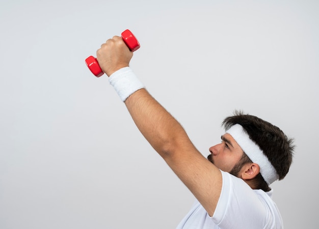 Teso giovane sportivo da uomo in piedi in vista di profilo che indossa la fascia e il braccialetto che esercitano con con manubri isolato su bianco con spazio di copia