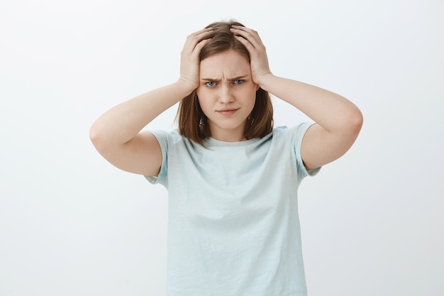 Testa che gira dal lavoro in ritardo per la scadenza. Ritratto di donna carina interessata stanca e turbata con capelli castani arricciati che increspa le labbra accigliate e che guardano intensamente tenendo le mani sulla testa