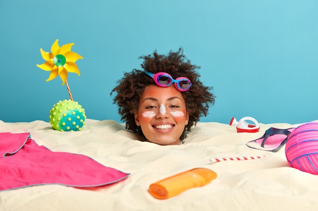Testa di giovane donna con crema solare sul viso circondato da accessori da spiaggia