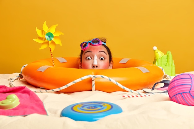 Testa di giovane donna con crema solare sul viso circondato da accessori da spiaggia