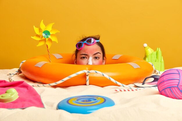 Testa di giovane donna con crema solare sul viso circondato da accessori da spiaggia