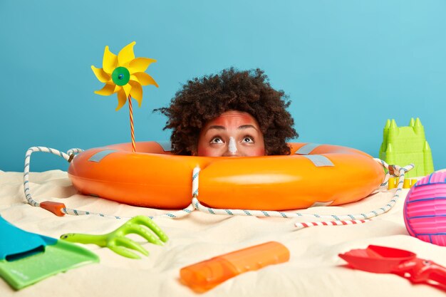 Testa di giovane donna con crema solare sul viso circondato da accessori da spiaggia