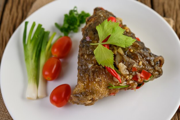 Teste di pesce fritte condite con peperoncini rossi su un piatto bianco con pomodori e cipollotti.