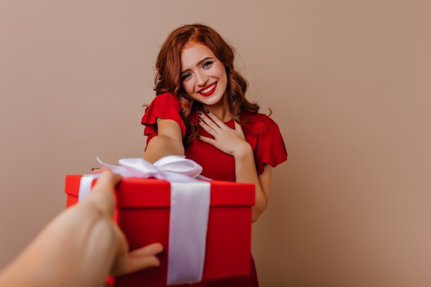 Timida bella ragazza in abito rosso in posa per il suo compleanno. Foto interna di donna riccia ispirata con regalo di capodanno.