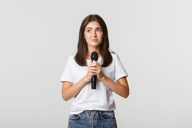 Timida ragazza bruna carina spaventata di cantare in pubblico, in piedi con il microfono e con aria nervosa.