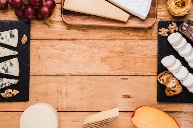 Tipi di formaggio; uva; noce e pasta disposti in cornice su una superficie di legno