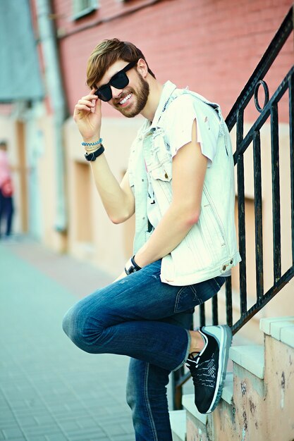 Tirante bello sorridente divertente dell'uomo bello dei pantaloni a vita bassa in panno alla moda di estate nella via in occhiali da sole