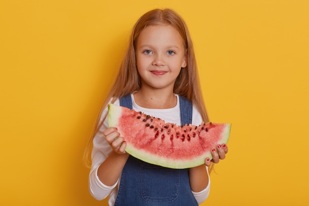 Tiro al coperto di bambina affascinante con porzione di anguria dolce nelle sue mani