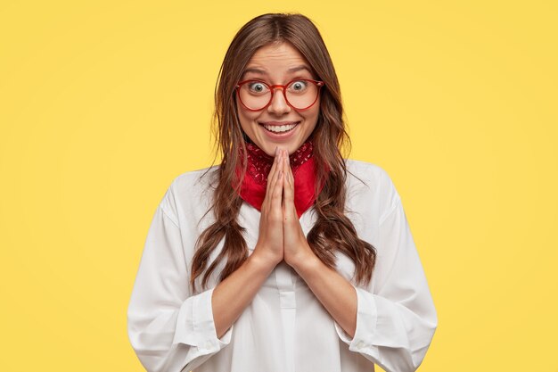 Tiro al coperto di donna felice felice ha un sorriso affascinante, tiene le mani in gesto di preghiera