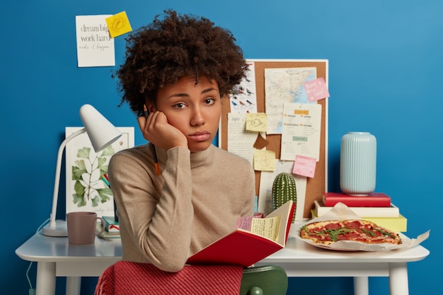 Tiro al coperto di ragazza afro sconvolta ha l'espressione del viso triste, tiene il taccuino aperto, stanco della preparazione all'esame