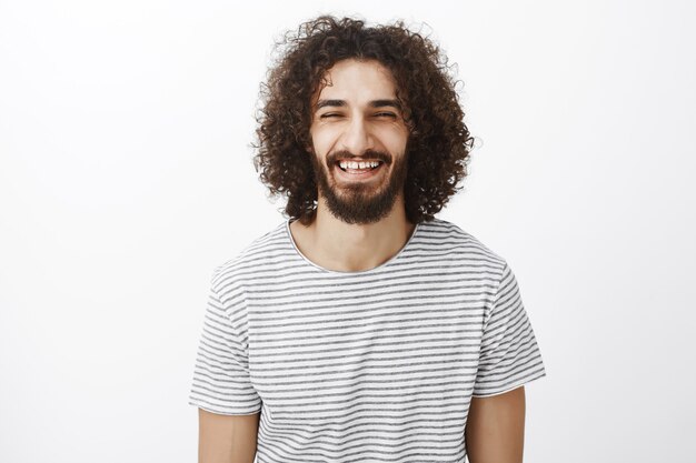 Tiro al coperto di un ragazzo simpatico e giocoso in camicia a righe alla moda, strizzare gli occhi e ridere ad alta voce, sentire qualcosa di divertente e godersi una splendida giornata di sole primaverile