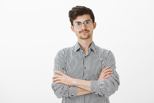 Tiro al coperto di un uomo europeo intenso dispiaciuto con barba e baffi in occhiali alla moda, tenendo le mani incrociate sul petto e guardando con attesa, offeso e volendo sentire le scuse