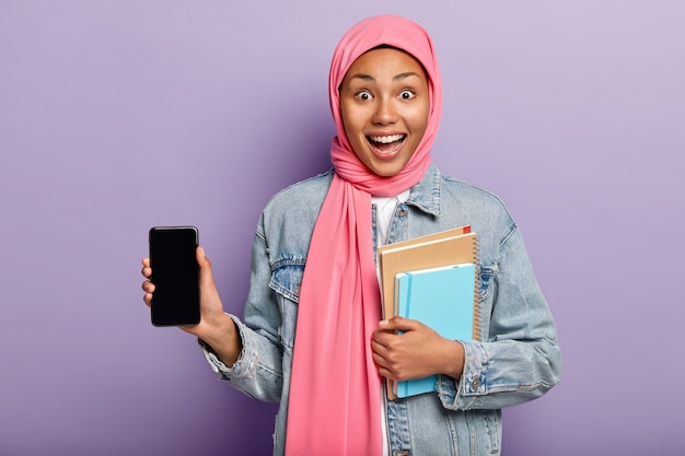 Tiro al coperto di una donna musulmana ottimista dalla pelle scura introduce un fantastico gadget
