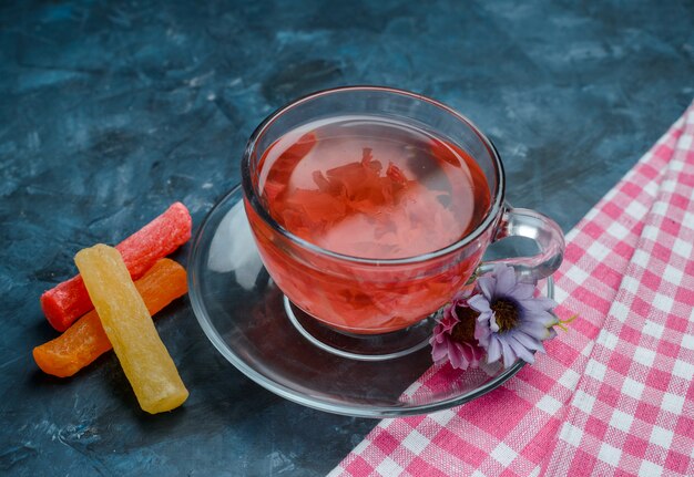 Tisana con caramelle, fiori in una tazza su blu e strofinaccio, vista dell'angolo alto.