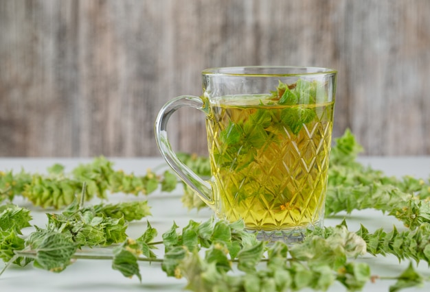 Tisana con foglie in una tazza di vetro su bianco e sgangherata,